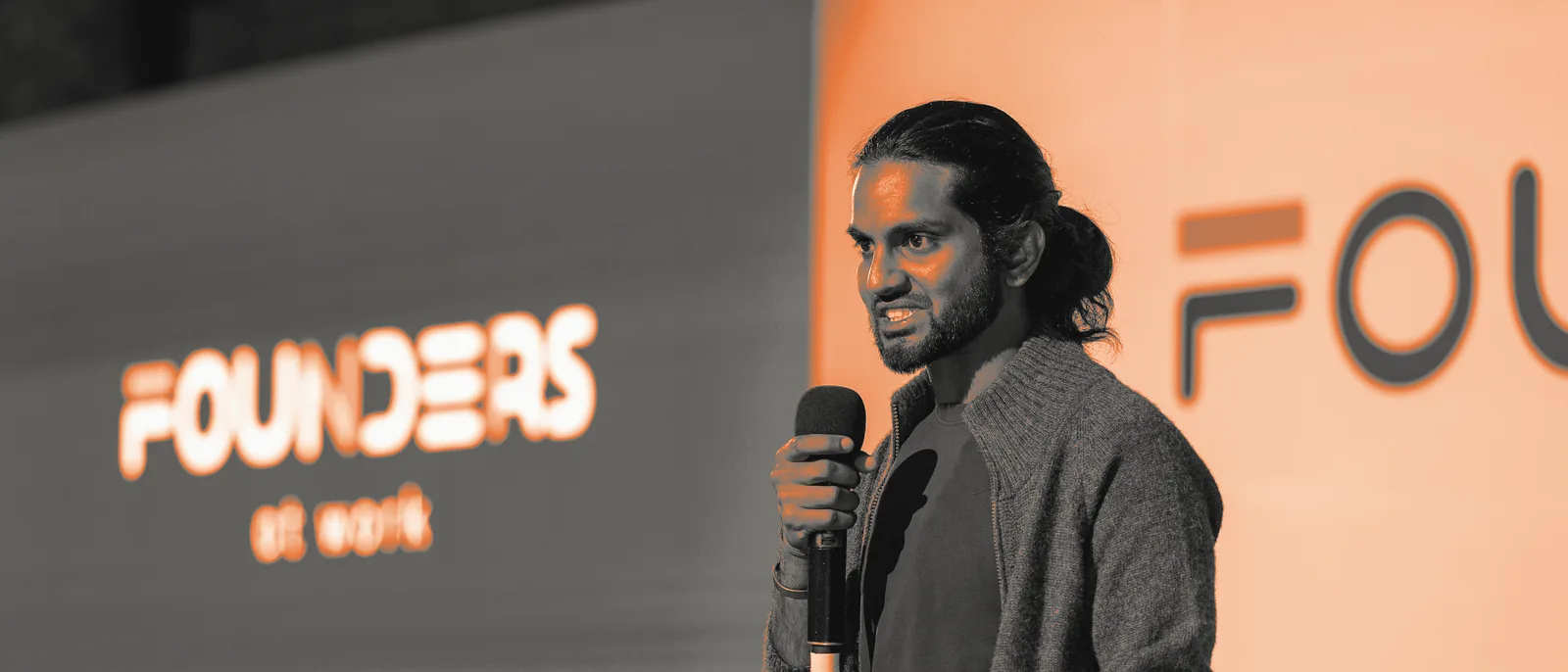Keshav Mohabir mid-talk on the Founders at Work Summit stage, the event logo on the screen behind him